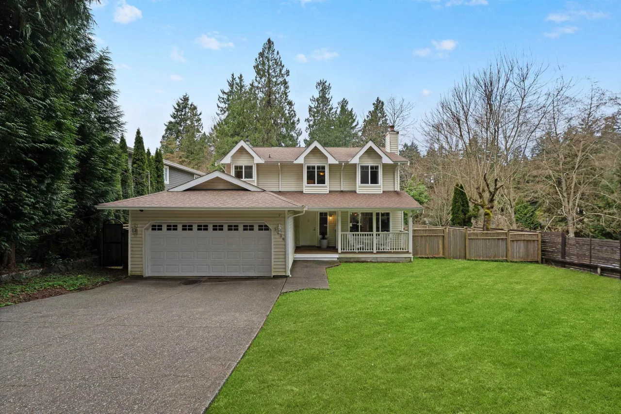 Two-story west coast home framed by evergreens with a manicured lawn at Eagle Harbour